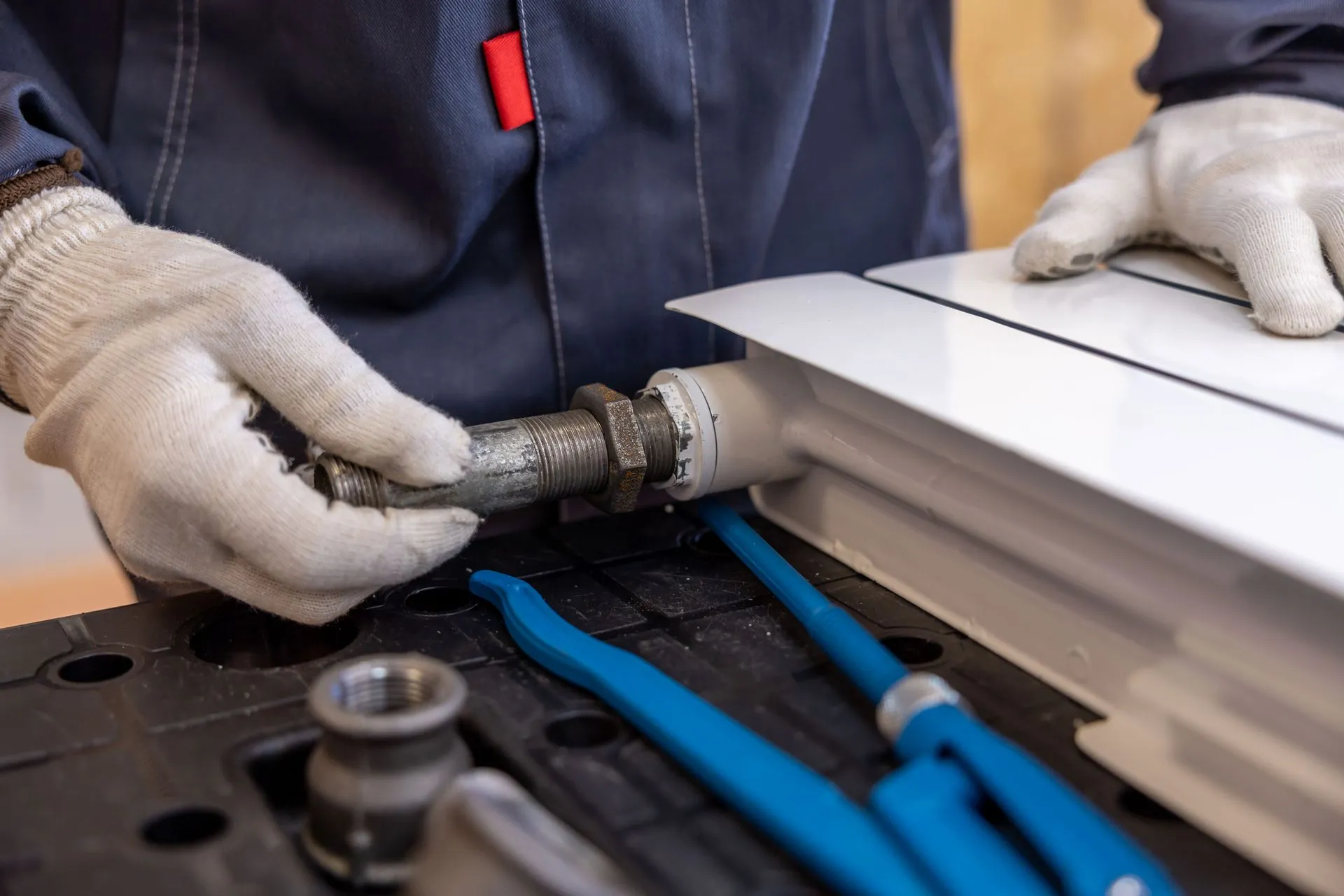 Plumber fitting a radiator valve, pipe wrenches laid out beside them